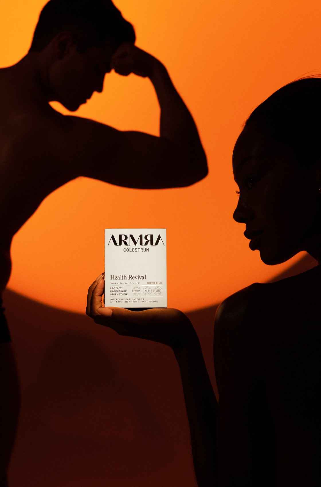 Two silhouetted figures holding an ARMRA box against orange light