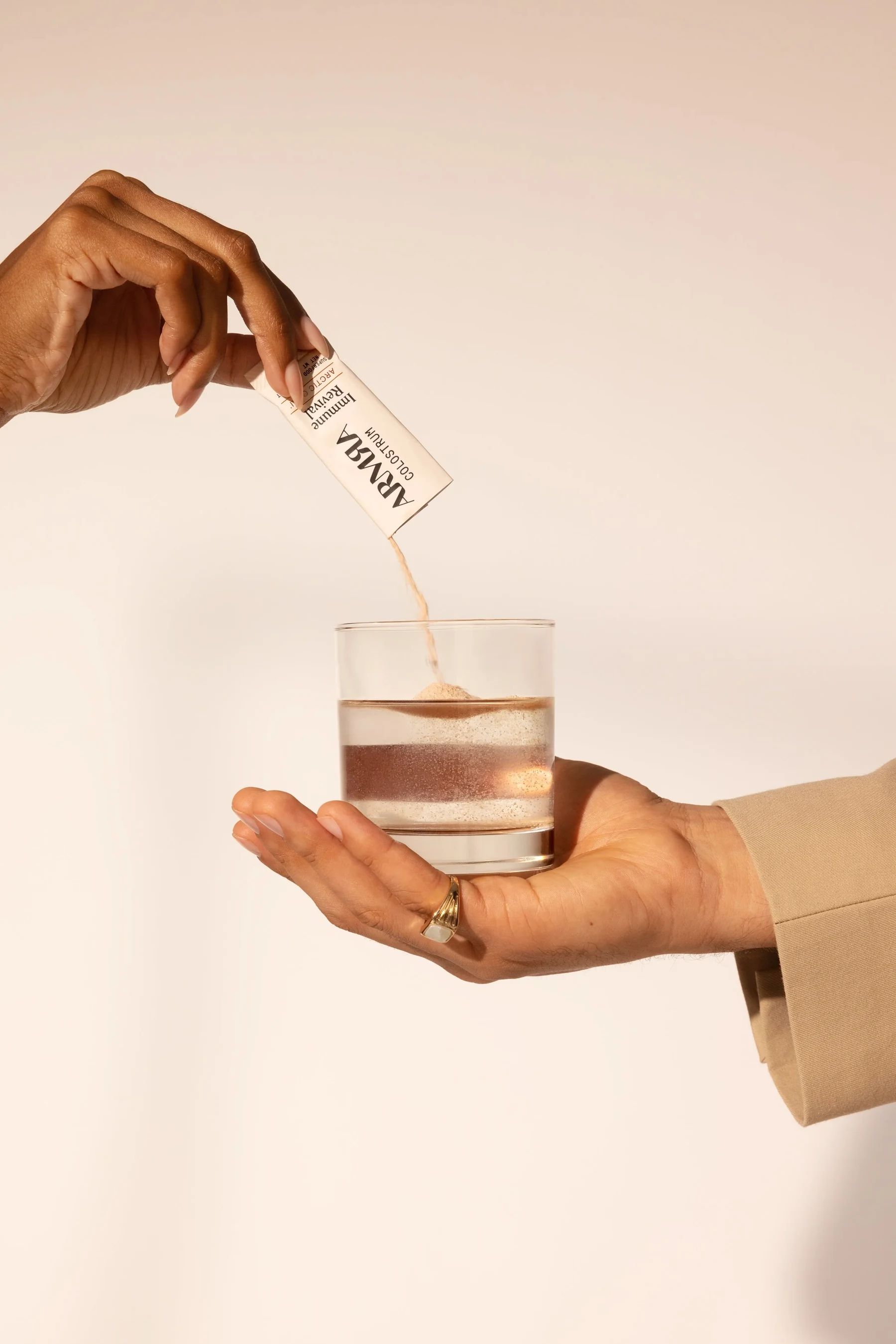 Hand pouring an ARMRA stick pack into a glass of water