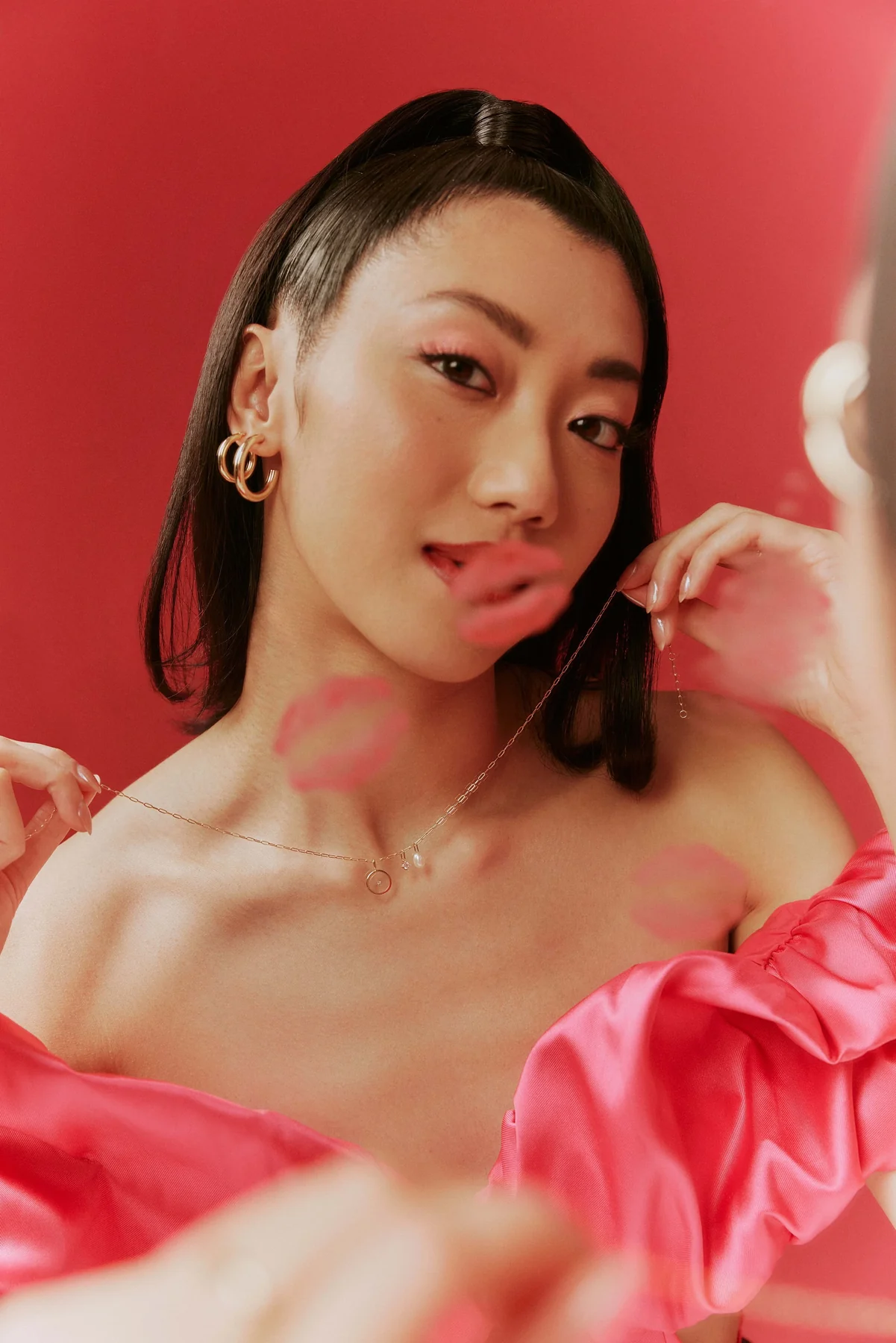Model in pink satin wearing gold earrings, looking over her shoulder against red