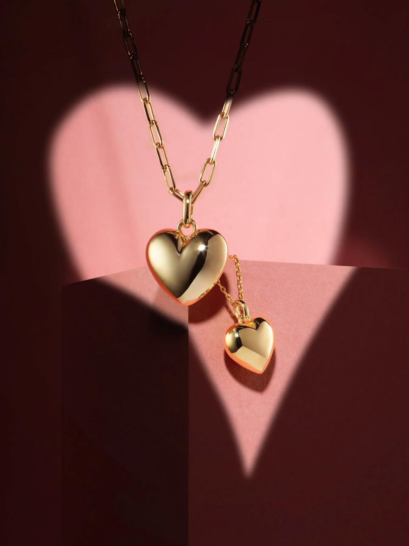 Gold heart pendant lit by a heart-shaped light on dark red