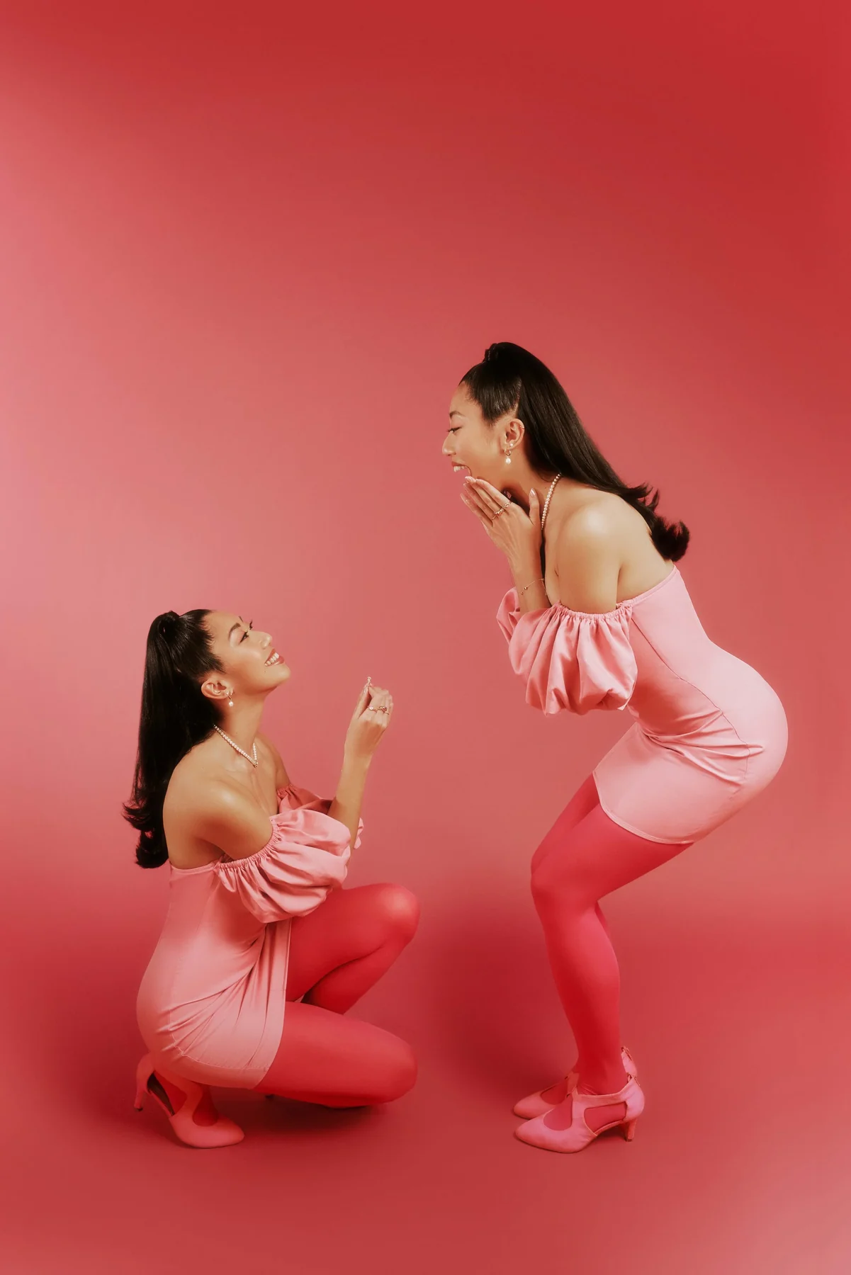 Two models in pink on a red set, one kneeling in a mock proposal