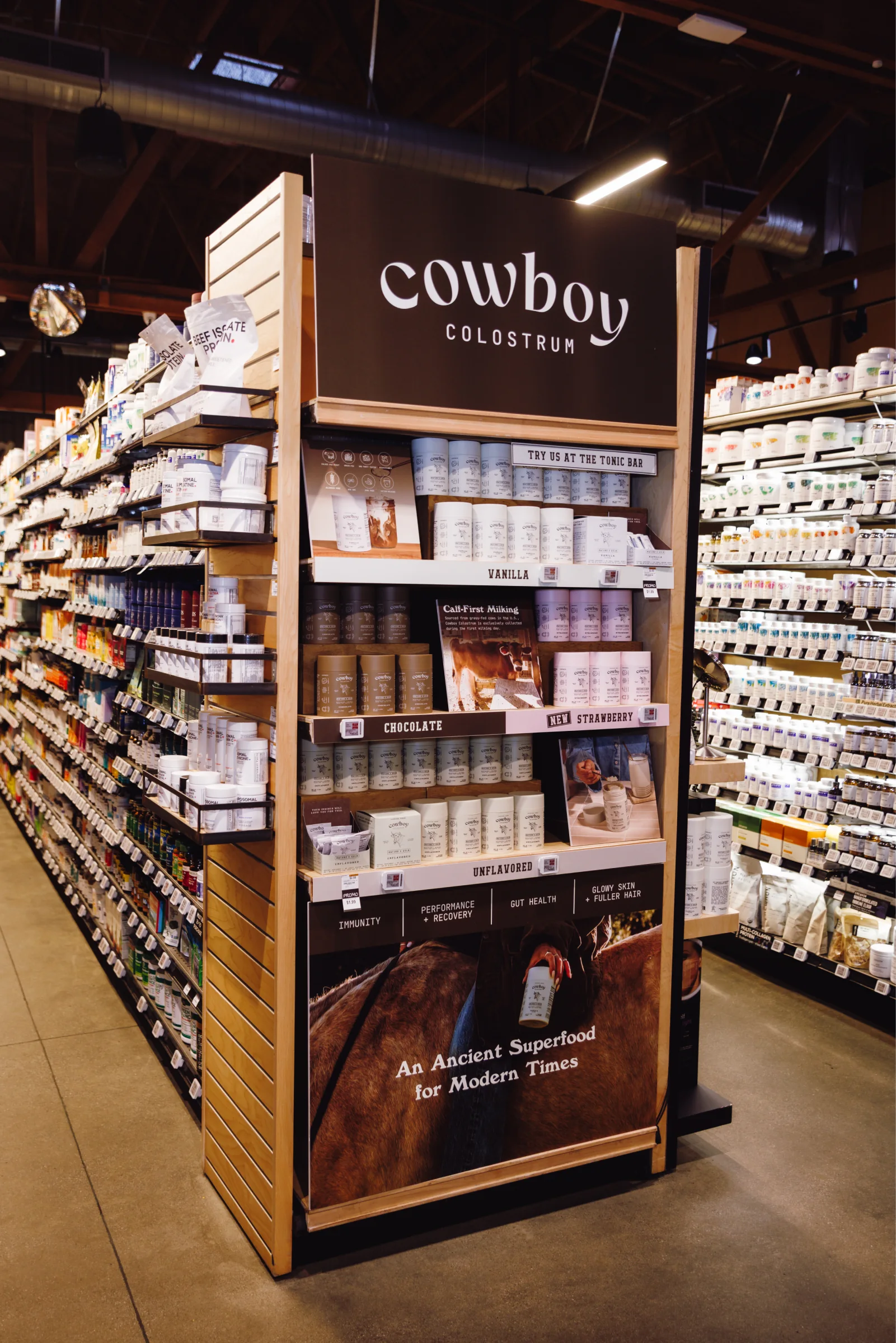 Cowboy Colostrum end cap in an Erewhon aisle: wordmark header, flavor shelves and “An Ancient Superfood for Modern Times” at the base