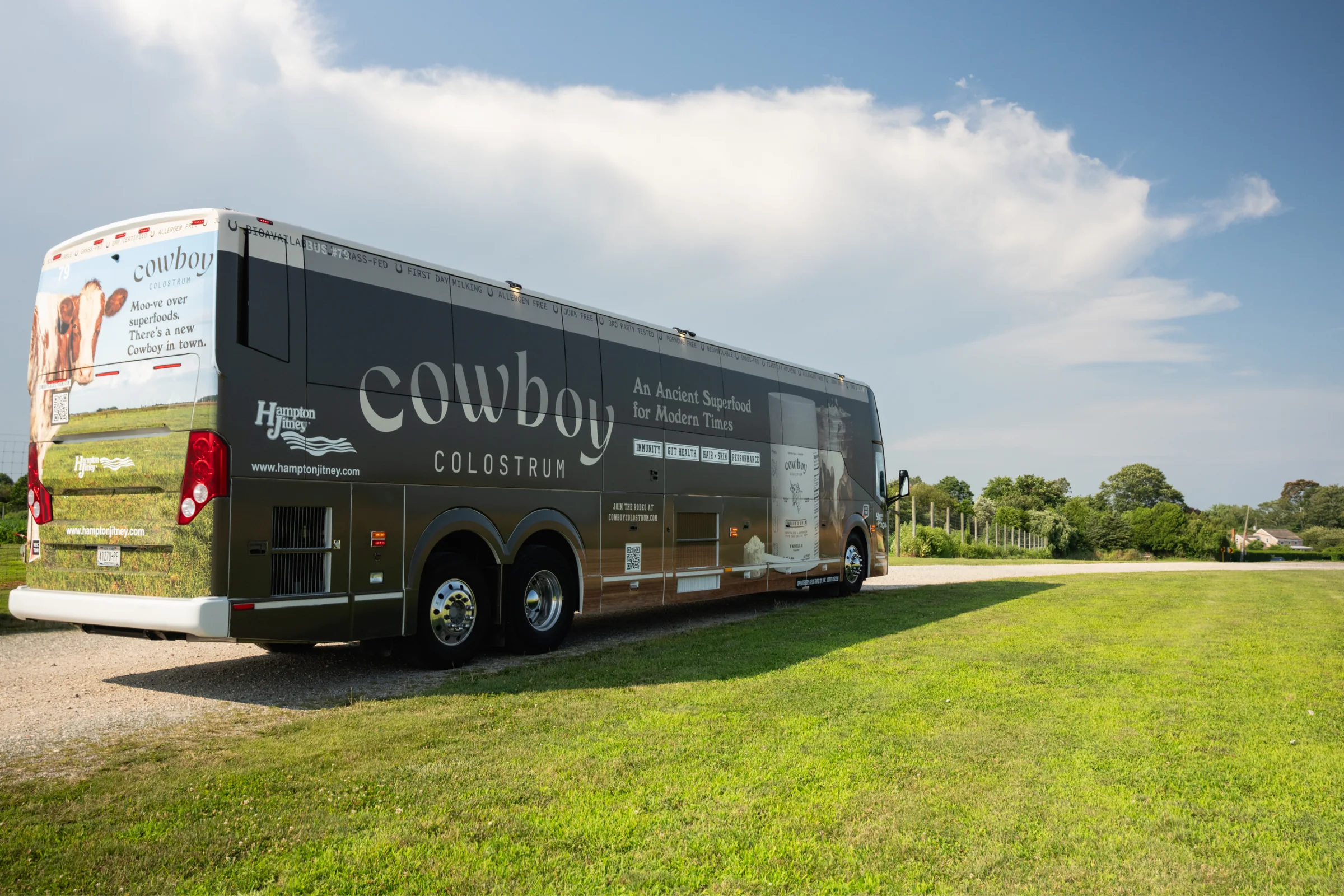 The wrapped coach parked on grass: the Cowboy wordmark, “An Ancient Superfood for Modern Times” and a cow on the rear
