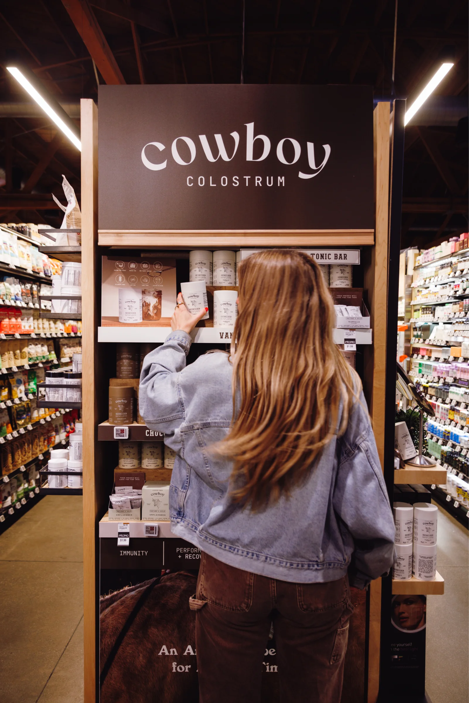 A shopper in a denim jacket takes a tub from the Cowboy Colostrum end cap