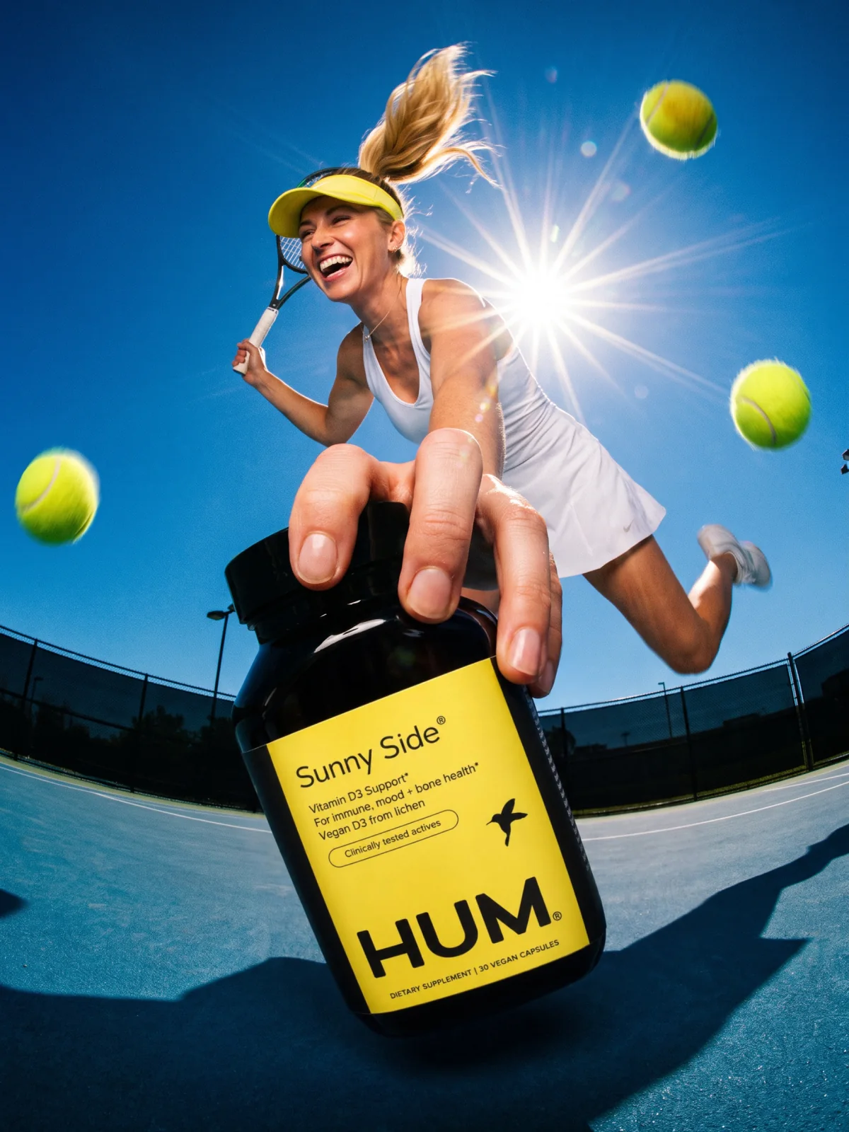 A tennis player mid-jump on a court holding a Sunny Side bottle toward the camera, balls in the air