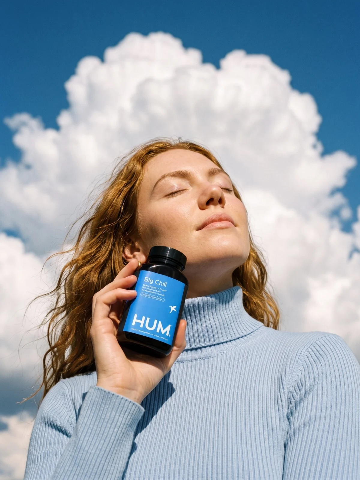 Woman with eyes closed against a big white cloud, holding a blue Big Chill bottle to her cheek