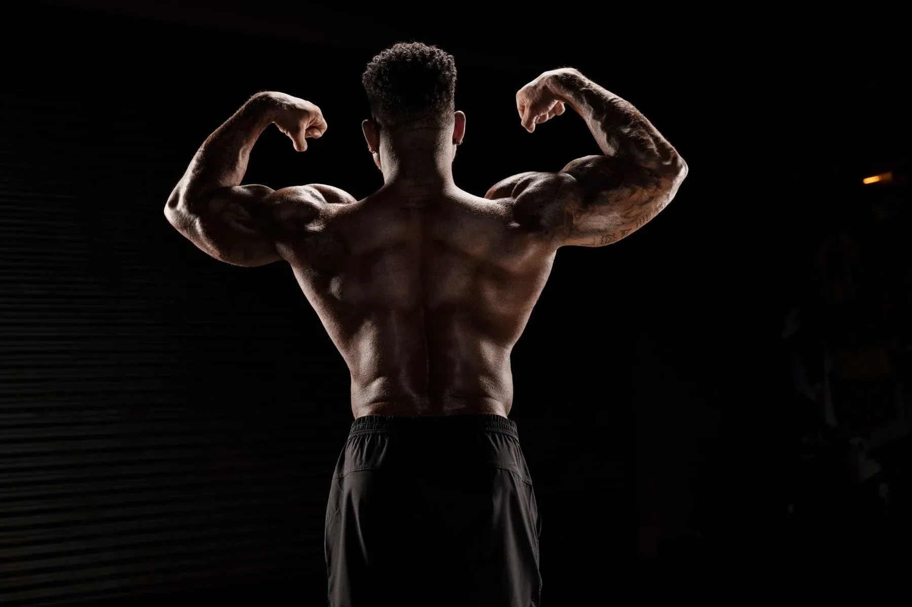 Shaun T from behind in a back double-biceps pose against black